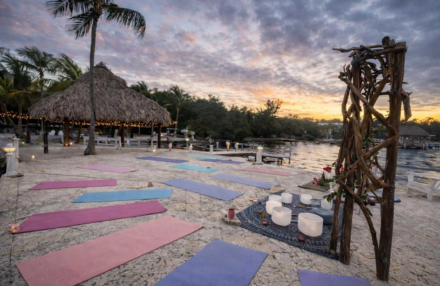 Waterfront sunset yoga setup at Largo Resort in Key Largo Florida with colorful mats, crystal singing bowls, tiki hut, and calm bay waters at dusk.