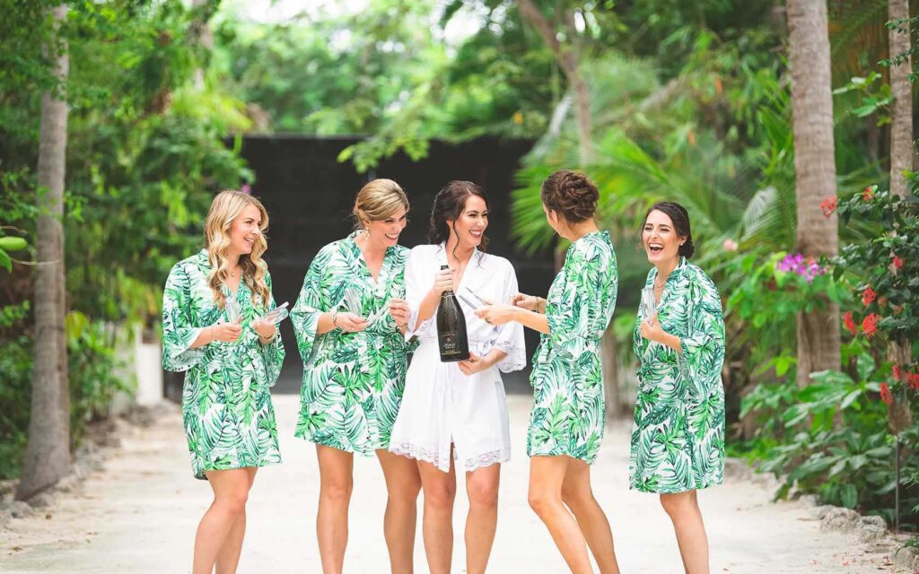 Bride and bride's maids in matching robes opening a bottle of champagne